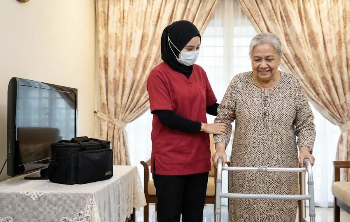 Testimoni Pelanggan Physiomobile: Rawatan Fisioterapi dengan Penjagaan Prihatin 2 Ahli fisioterapi wanita membimbing pesakit wanita berlatih berjalan dengan alat bantuan di rumah
