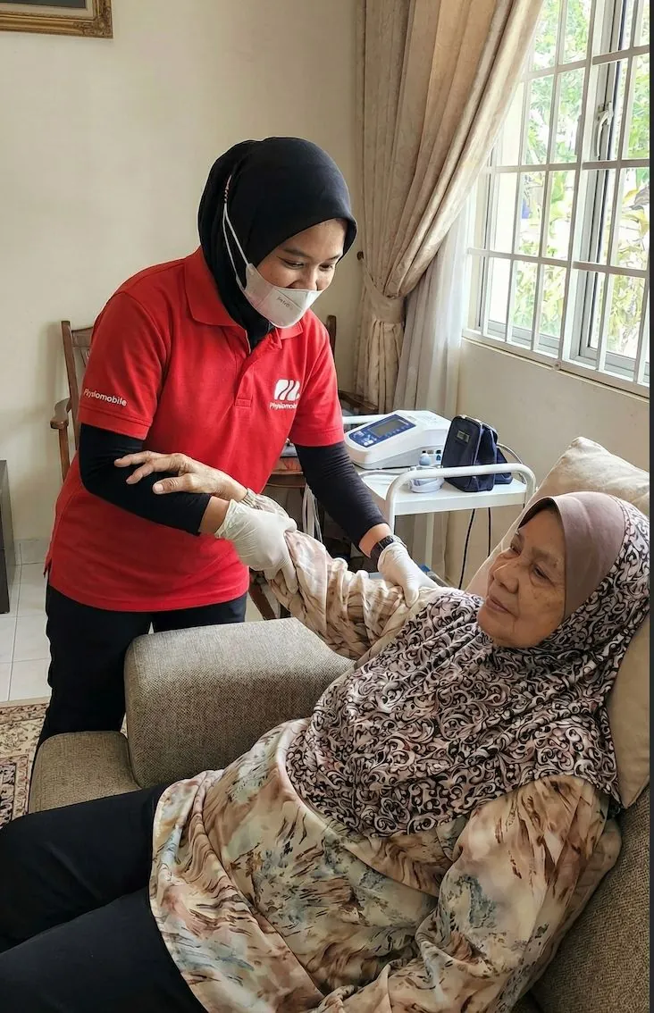 Ahli fisioterapi wanita menilai pergerakan lengan pesakit wanita warga emas di rumah