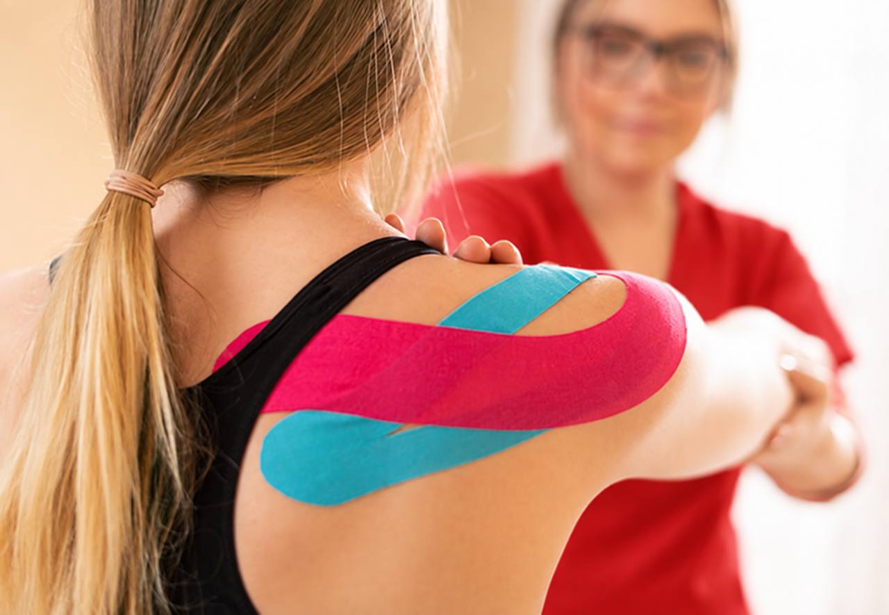 Sakit Bahu Akibat Dislocate: Apa Yang Fisioterapi Boleh Bantu? 4 Fisioterapis memasang kinesiology tape pada bahu pesakit sebagai sebahagian daripada rawatan sokongan